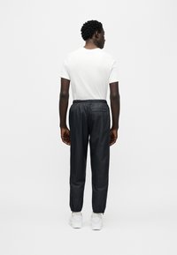 Μαύρο αθλητικό παντελόνι με ελαστική μέση και φερμουάρ στους αστραγάλους, σε συνδυασμό με λευκό απλό μπλουζάκι και λευκά αθλητικά παπούτσια, από πίσω.