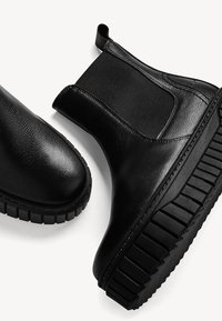 Svarta läderankelboots med elastiska sidopaneler, rund tå och strukturerad gummisula för ökad dragkraft och stabilitet.