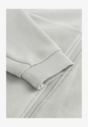 Lys grå sweatshirtstof med en tekstureret overflade, der har ribbede manchetter og en synlig lynlås langs kanten, hvilket fremhæver et holdbart design.