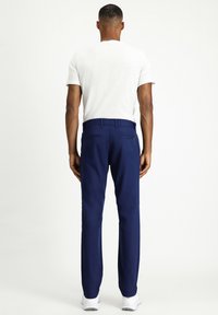 Pantalones azul marino hechos de una tela suave, diseño de pierna recta, con dos bolsillos traseros, combinados con una camiseta blanca lisa y zapatos blancos.