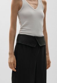 Débardeur blanc à côtes et pantalon noir taille haute avec un détail de taille repliée. Le tissu semble lisse et léger.