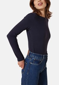 Marineblaues Langarmshirt mit Rundhalsausschnitt, kombiniert mit hoch taillierten blauen Jeans mit Front- und Gesäßtaschen.