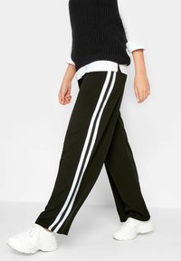 Czarne spodnie o szerokich nogawkach z białymi paskami po bokach, wykonane z miękkiego materiału. W połączeniu z czarnym swetrem bez rękawów i białymi sneakersami.