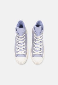 Zapatillas altas de lona en color morado claro con puntera de goma blanca y cordones, que cuentan con un cuello acolchado y un detalle del logo en el costado.