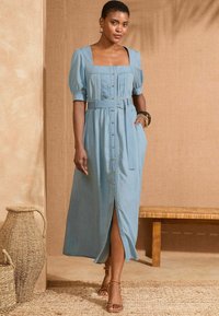 Light blue, long denim dress with short puff sleeves, square neckline, front button closure, and a tied waist belt. Features side pockets.