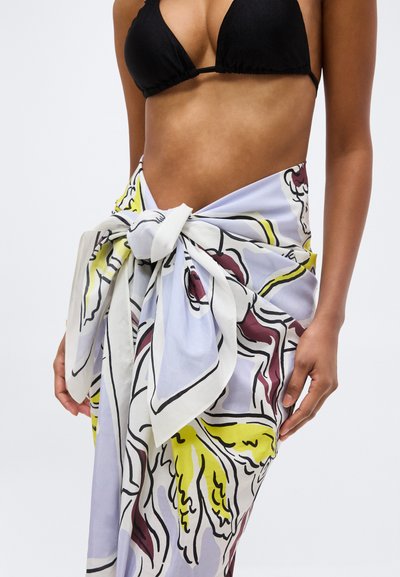 Γυναίκα με μαύρο τοπ μπικίνι και πολύχρωμη παρεό δεμένη στη μέση με αφηρημένα μοτίβα σε κίτρινο, λευκό και βουργουνδί.