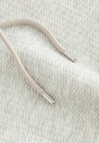 Lys grå stof med et herringbone mønster, der har en beige snor med sølvmetal spidser. Blød tekstur og subtil glans.