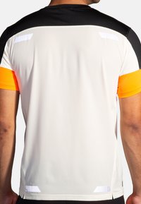Camisa deportiva de manga corta con un cuerpo blanco, hombros negros y mangas naranjas. Detalles notables incluyen un tejido texturizado y acentos reflectantes.