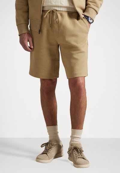 Shorts beige in misto cotone con vita elastica e cordoncino, dotati di tasche laterali e una vestibilità comoda, abbinati a sneakers beige.