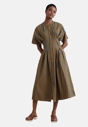 Gestreiftes Midi-Kleid in Blau und Gelb, mit Knopfleiste vorne, kurzen Ärmeln und weit schwingendem Rock mit Raffung. Holz-Absatzclogs werden getragen.