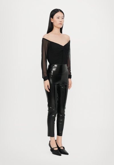 Sort off-the-shoulder top med knude-detail, parret med højtaljede sorte latexbukser og spidse flade sko med sløjfede detaljer.
