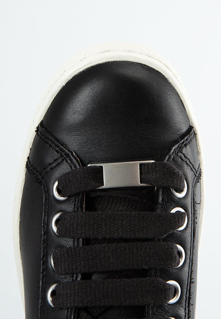 Zapatilla de cuero negra con punta redonda, cordones negros, ojetes plateados y suela de goma blanca. Presenta un acento metálico en los cordones.