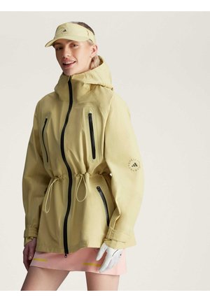 Chaqueta impermeable amarilla con cintura ajustada, múltiples bolsillos con cremallera en negro y capucha. También es visible una visera a juego.
