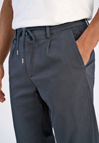 Pantalons gris foncé en tissu lisse, dotés d'une taille à cordon, de poches sur les côtés et d'une coupe décontractée avec des détails de couture simples.