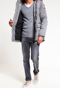 Graue gepolsterte Jacke mit schwarzem Futter, grauem Pullover und grauen Jeans. Helle beige Sneakers. Dekorative Nähte auf der Jacke.