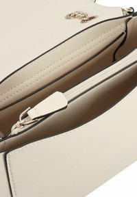 Interno di una borsa color beige con una texture liscia, dotata di una tasca con zip e un accento in catena dorata sul flap esterno. Dettagli con cuciture nere.