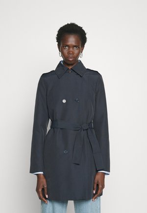 Marineblå trenchcoat med dobbeltradet knappelukking, belte i midjen, skulderepaulettes og lange ermer. Glatt stoff med svak glans.