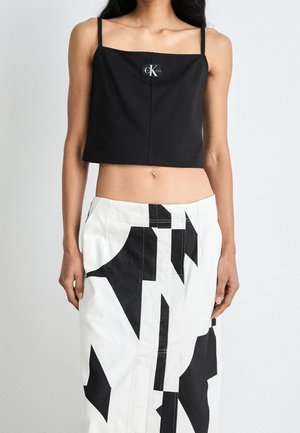Kobieta nosząca czarny krótki top z logo Calvin Klein oraz białą spódnicę z wysokim stanem z wyraźnymi czarnymi, abstrakcyjnymi wzorami.