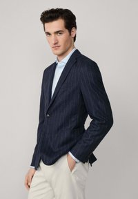 Sako s námořnickým pruhem, slim fit, s jedním knoflíkem a klopovými límci. Doplněno světle modrou košilí pod ním.