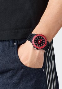 Must mustriga kell musta kummist korviga ja musta näoga, millel on valged tunni markerid ja käed, kantud randmel denimkangaga.