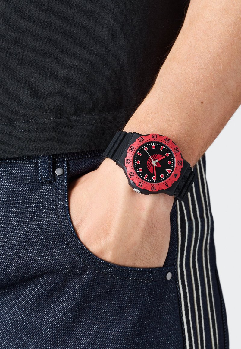 Must mustriga kell musta kummist korviga ja musta näoga, millel on valged tunni markerid ja käed, kantud randmel denimkangaga.