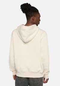 Felpa beige con cappuccio grande, polsini e orlo a coste, morbida al tatto e dalla vestibilità comoda, indossata sopra jeans blu.