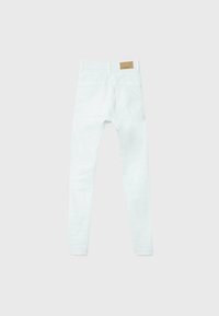 Jean skinny blanc vu de dos avec deux poches et une étiquette de marque en cuir marron clair sur la ceinture, sur un fond gris clair.