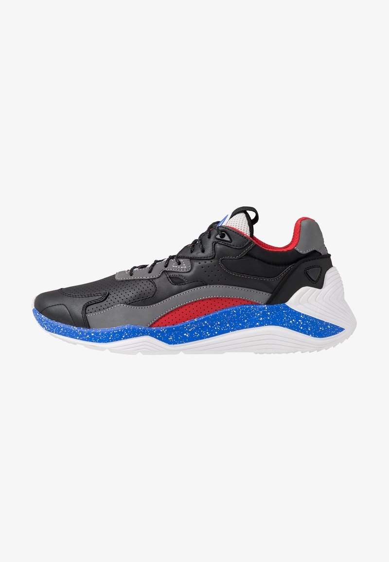 Chaussure de sport noire, grise et rouge avec une semelle intermédiaire tachetée de bleu et une semelle blanche, dotée d’une fermeture à lacets et d’un col rembourré à la cheville.
