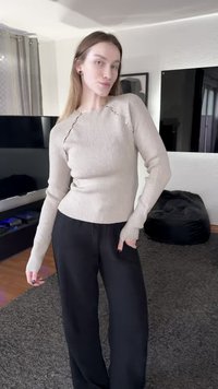 Beige ribbed sweater with long sleeves, featuring cut-out details on the shoulders and fitted design, paired with loose black pants.