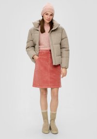 Beige Pufferjacke, pinkes geripptes Sweater und korallenfarbener Cordrock. Beige Stiefeletten mit dicker Sohle, tansfarbene Strickmütze mit Streifen.