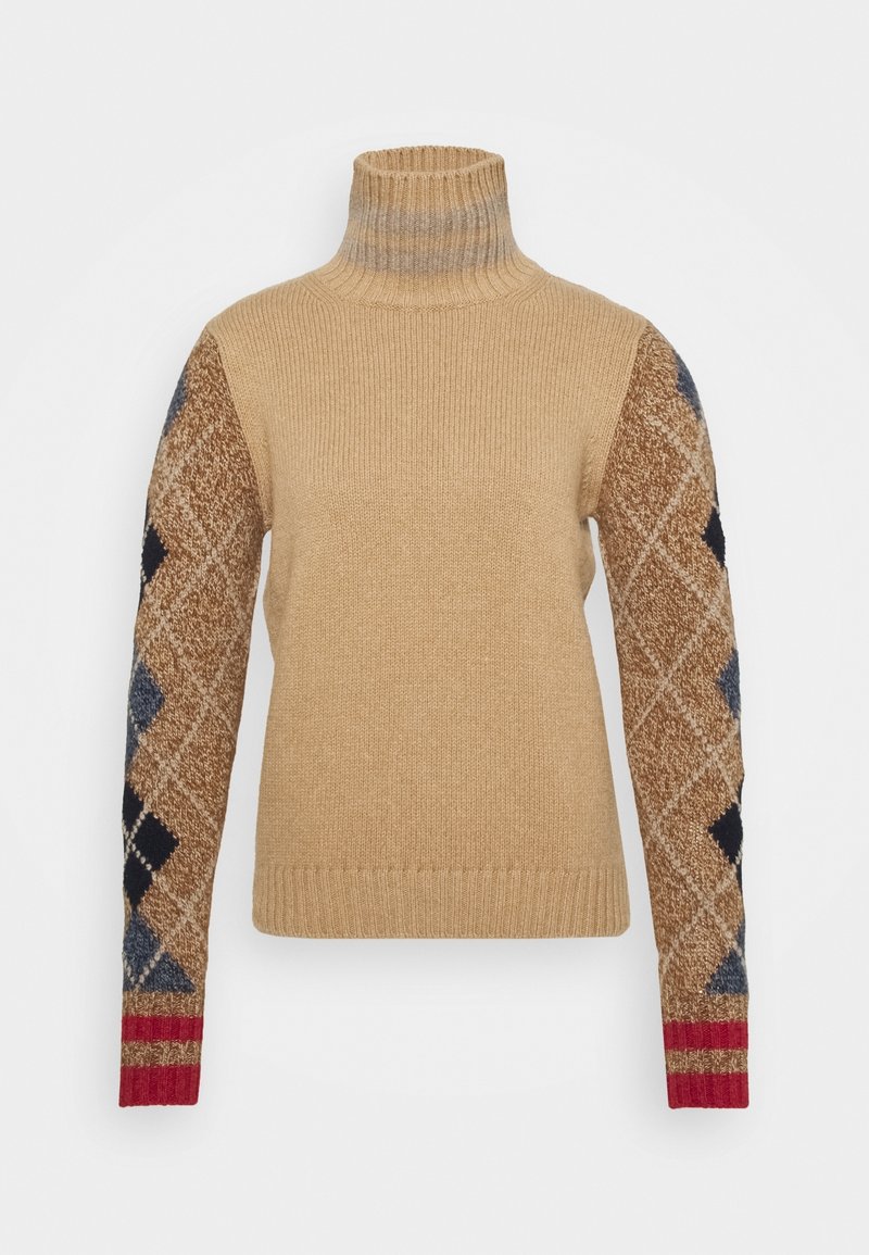 Pull à col roulé beige en maille avec texture côtelée ; une manche présente un motif de losanges marron et bleu, terminé par un accent rouge au poignet.