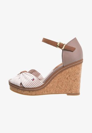 Sandalia con cuña y suela de corcho, talón de tela beige, correa marrón en el tobillo con hebilla dorada, y lazo delantero de rayas beige y blancas con pequeño logotipo.
