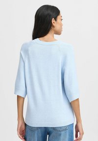 Světle modrý, měkký pletený svetr s kulatým výstřihem, krátkými rukávy a ribkovaným lemem; má viditelné švy na ramenou.