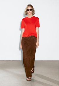 Camicetta rossa a maniche corte, gonna in cotone a coste marrone e sandali neri. Design semplice, taglio dritto. Texture liscia, senza motivi visibili.