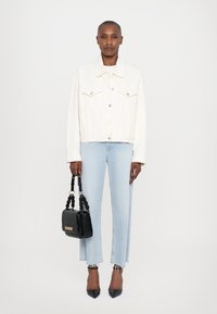White denim jacket, light blue straight-leg jeans with frayed hem, black square handbag with knotted handle, and pointed black heels.