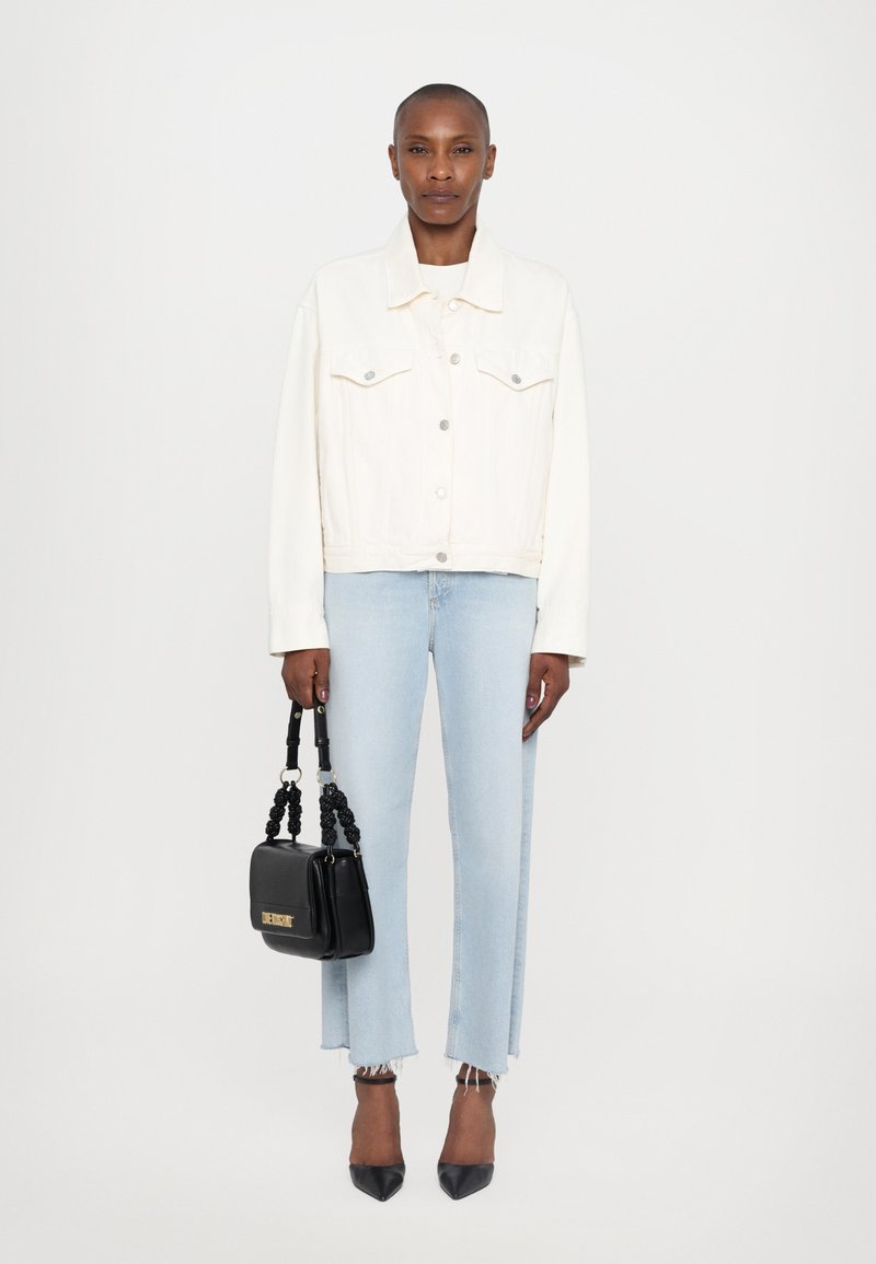 White denim jacket, light blue straight-leg jeans with frayed hem, black square handbag with knotted handle, and pointed black heels.