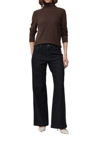 Maglione dolcevita marrone leggero con sottili scintillii, abbinato a jeans larghi in denim scuro a vita alta. I stilosi tacchi bianchi completano il look.