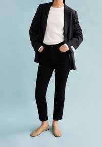 Jean noir taille haute associé à un haut blanc ajusté et un blazer noir à fines rayures, cintré. Chaussures beige à enfiler.