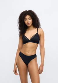 Σετ μαύρου εσωρούχου που περιλαμβάνει ένα τριγωνικό μπουστάκι με δαντελένιο τελείωμα και ρυθμιζόμενες τιράντες, συνδυασμένο με μαγιό σλιπ ψηλής μέσης. Λείο ύφασμα.
