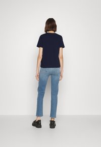 Námorně modré bavlněné tričko s krátkými rukávy, spárované se světle modrými slim-fit džíny a černými botami s robustní podrážkou, pohled zezadu.