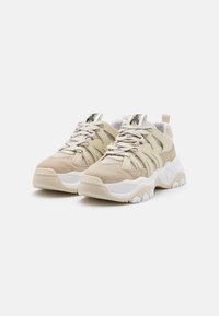 Beige sneakers med en blanding av mesh og semsket skinn. Tykk hvit gummisåle med teksturerte detaljer. Snøring i kryssmønster og merkevarelogo på tungen.