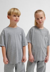 To børn har matchende grå bomulds-T-shirts med korte ærmer. Hver skjorte har et lille blåt broderet logo på venstre bryst.