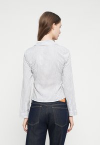 Csíkos gombos ing könnyű anyagból, gallérral, hosszú ujjakkal és rövidített szabással; sötét farmernadrággal párosítva.