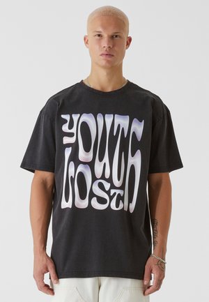 Schwarzes Baumwoll-T-Shirt mit fettem, welligem weißen und lila Text, der "YOUTH LOST" auf der Vorderseite zeigt. Lockerer Schnitt und kurze Ärmel.