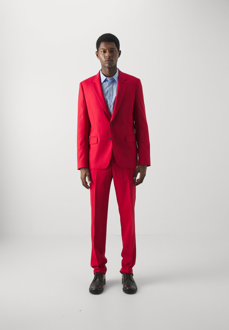 Rød jakkesæt med en tætsiddende blazer og matchende bukser, parret med en lyseblå skjorte. Glat stof, klassiske klapkraver og sidelommer.