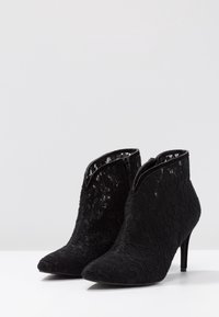 Bottes de cheville en dentelle noire avec un bout pointu et un talon aiguille. Elles possèdent une fermeture éclair et un motif floral sur toute la surface.