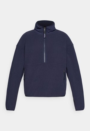 Pulover din fleece de culoare bleu marin, cu guler înalt, închidere cu jumătate de fermoar și două buzunare laterale cu fermoar. Are o croială lejeră și o textură moale.