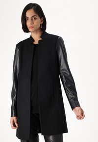 Black coat with a wool body and leather sleeves. Features a straight cut, no closure, and minimalistic design without embellishments.
