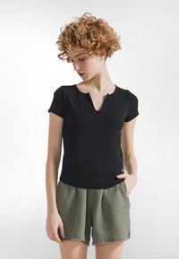 Černý top s krátkým rukávem a výstřihem do V s žebrovanou strukturou, doplněný světle zelenými šortkami s texturou, třepenými lemy a postranními kapsami.