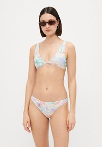 Flerfarget bikini-sett med trekantstopp og lavt utskårne bukser. Laget av glatt stoff med et tropisk blomstermønster i pastellfarger.